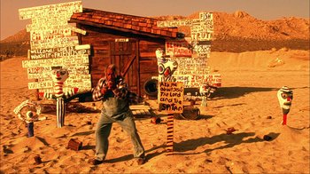 Movie still from “House of 1000 Corpses” (2003), directed by Rob Zombie – A man holding a baseball bat in the middle of a desert; Wide shot, Low angle
