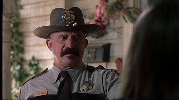 Movie still from “House of 1000 Corpses” (2003), directed by Rob Zombie – A man in a police uniform is looking at the camera; Close Up shot, Over the shoulder angle
