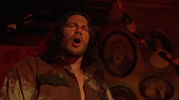 Movie still from “House of 1000 Corpses” (2003), directed by Rob Zombie – A man with long black hair is singing; Close Up shot, Low angle