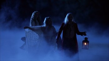 Movie still from “House of 1000 Corpses” (2003), directed by Rob Zombie – A group of three women walking through the fog holding a lantern; Wide shot, Low angle