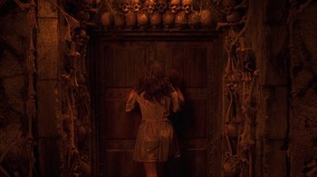 Movie still from “House of 1000 Corpses” (2003), directed by Rob Zombie – A woman standing in front of a door with skulls around it; Wide shot, High angle