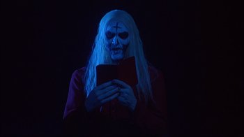 Movie still from “House of 1000 Corpses” (2003), directed by Rob Zombie – A person in a costume holding a cell phone; Medium shot, Low angle