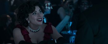 Movie still from “House of Gucci” (2021), directed by Ridley Scott – A woman in a red dress sitting at a table; Close Up shot, Over the shoulder angle