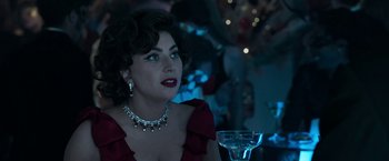 Movie still from “House of Gucci” (2021), directed by Ridley Scott – A woman in a red dress sitting in front of a glass of water; Close Up shot, Over the shoulder angle