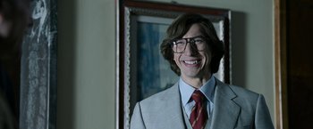 Movie still from “House of Gucci” (2021), directed by Ridley Scott – A man in a suit and tie smiling for the camera; Medium shot, Low angle