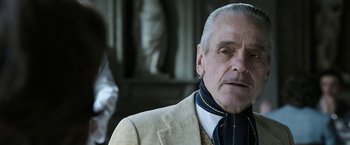 Movie still from “House of Gucci” (2021), directed by Ridley Scott – An older man in a beige suit and a blue neck tie; Close Up shot, Low angle