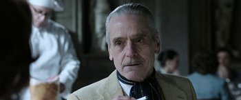 Movie still from “House of Gucci” (2021), directed by Ridley Scott – An older man in a suit and tie holding a cigarette in his mouth; Close Up shot, Low angle