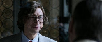 Movie still from “House of Gucci” (2021), directed by Ridley Scott – A man in a suit and glasses is smiling for the camera; Close Up shot, Over the shoulder angle
