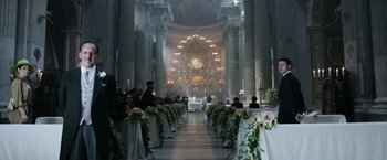 Movie still from “House of Gucci” (2021), directed by Ridley Scott – People sitting at tables in a large cathedral; Extreme Wide shot, High angle