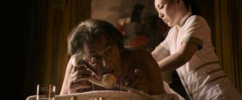 Movie still from “House of Gucci” (2021), directed by Ridley Scott – An old man talking on a phone while a woman looks on; Medium shot, High angle