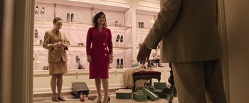 Movie still from “House of Gucci” (2021), directed by Ridley Scott – A woman in a red dress is standing in front of a man in a brown suit; Medium shot, Over the shoulder angle