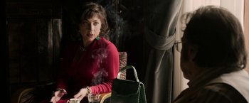 Movie still from “House of Gucci” (2021), directed by Ridley Scott – A woman sitting in front of a green purse; Medium shot, Over the shoulder angle