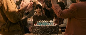 Movie still from “House of Gucci” (2021), directed by Ridley Scott – A young boy sitting in front of a birthday cake; Medium shot, Over the shoulder angle