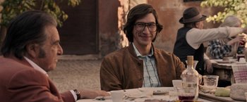 Movie still from “House of Gucci” (2021), directed by Ridley Scott – A man sitting at a table with papers in front of him; Medium shot, Over the shoulder angle