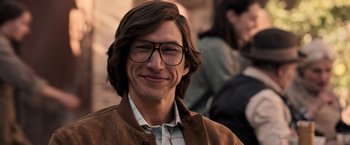 Movie still from “House of Gucci” (2021), directed by Ridley Scott – A man with long brown hair wearing glasses and a brown jacket; Close Up shot, Over the shoulder angle