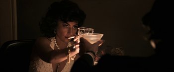 Movie still from “House of Gucci” (2021), directed by Ridley Scott – A woman is holding a martini glass and smoking a cigarette; Close Up shot, Over the shoulder angle