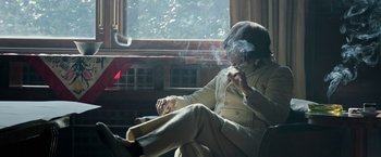Movie still from “House of Gucci” (2021), directed by Ridley Scott – A man sitting in front of a window smoking a cigarette; Medium shot, Low angle