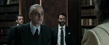 Movie still from “House of Gucci” (2021), directed by Ridley Scott – A man in a suit and tie standing next to another man in a suit and tie; Medium shot, Low angle