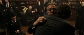 Movie still from “House of Gucci” (2021), directed by Ridley Scott – A man hugging another man in front of a group of people; Medium shot, Over the shoulder angle