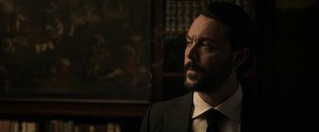 Movie still from “House of Gucci” (2021), directed by Ridley Scott – A man in a suit smoking a cigarette in a room; Close Up shot, Low angle