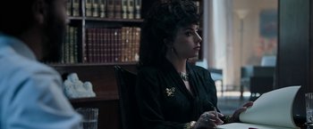 Movie still from “House of Gucci” (2021), directed by Ridley Scott – A woman sitting in a chair in front of a book case; Close Up shot, Over the shoulder angle