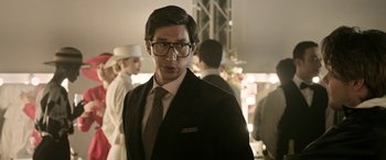 Movie still from “House of Gucci” (2021), directed by Ridley Scott – A man in a suit and tie standing next to other people; Close Up shot, Over the shoulder angle