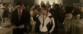 Movie still from “House of Gucci” (2021), directed by Ridley Scott – A young man in a white and black jacket drinking a beverage; Medium shot, Over the shoulder angle