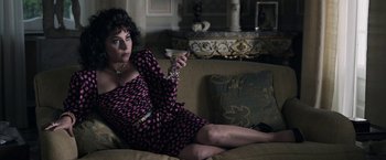 Movie still from “House of Gucci” (2021), directed by Ridley Scott – A woman is sitting on a couch holding a remote control; Medium shot, High angle
