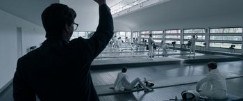 Movie still from “House of Gucci” (2021), directed by Ridley Scott – A man sitting on the floor of a gym with a skateboard; Wide shot, Low angle