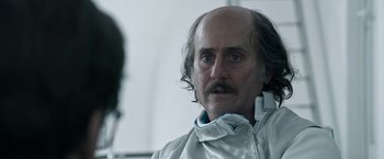 Movie still from “House of Gucci” (2021), directed by Ridley Scott – An older man with long hair and a mustache; Close Up shot, Over the shoulder angle