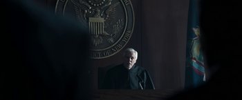 Movie still from “House of Gucci” (2021), directed by Ridley Scott – An older man in a black robe stands in front of a podium; Medium shot, Over the shoulder angle
