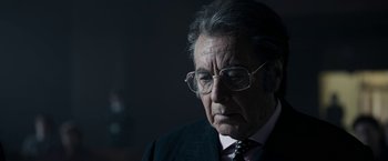 Movie still from “House of Gucci” (2021), directed by Ridley Scott – An older man wearing glasses and a suit and tie; Close Up shot, Over the shoulder angle