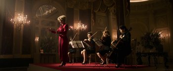 Movie still from “House of Gucci” (2021), directed by Ridley Scott – A group of people sitting in a room playing musical instruments; Wide shot, Low angle