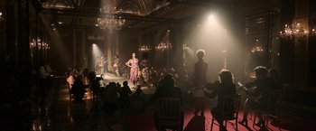 Movie still from “House of Gucci” (2021), directed by Ridley Scott – A group of people sitting and standing in a room; Extreme Wide shot, Over the shoulder angle