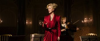 Movie still from “House of Gucci” (2021), directed by Ridley Scott – A woman in a red dress singing in a dark room; Medium shot, Over the shoulder angle