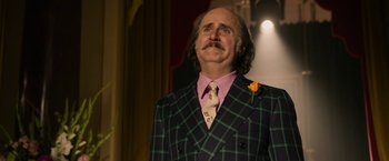 Movie still from “House of Gucci” (2021), directed by Ridley Scott – A man in a green and black suit and pink tie; Close Up shot, Low angle