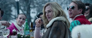 Movie still from “House of Gucci” (2021), directed by Ridley Scott – A woman smoking a cigarette while sitting at a table; Close Up shot, Over the shoulder angle