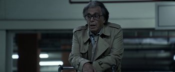 Movie still from “House of Gucci” (2021), directed by Ridley Scott – An older man wearing glasses sitting in a chair; Medium shot, Low angle