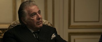 Movie still from “House of Gucci” (2021), directed by Ridley Scott – An older man sitting in a chair in front of a wall; Close Up shot, Over the shoulder angle