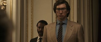Movie still from “House of Gucci” (2021), directed by Ridley Scott – A man in a suit and tie standing next to another man in a suit; Medium shot, Low angle