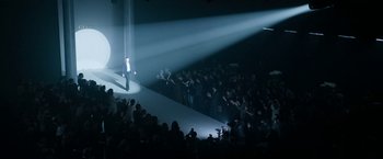 Movie still from “House of Gucci” (2021), directed by Ridley Scott – A man standing on a stage in front of an audience; Wide shot, High angle