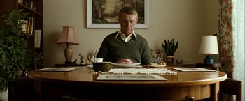 Movie still from “Hunger” (2008), directed by Steve McQueen – A man sitting at a dining room table looking at his cell phone; Medium shot, Low angle