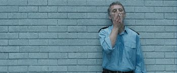 Movie still from “Hunger” (2008), directed by Steve McQueen – A man smoking a cigarette while leaning against a brick wall; Medium shot, Low angle