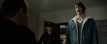 Movie still from “Hunger” (2008), directed by Steve McQueen – A man in a jean jacket standing in front of two other men; Medium shot, Over the shoulder angle