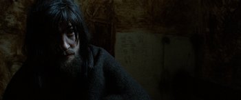 Movie still from “Hunger” (2008), directed by Steve McQueen – A man with long black hair sitting in a dark room; Close Up shot, High angle