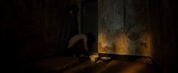 Movie still from “Hunger” (2008), directed by Steve McQueen – A person is sitting on the floor in a dark room; Wide shot, High angle