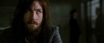Movie still from “Hunger” (2008), directed by Steve McQueen – A man with long hair and a beard looking to his left; Close Up shot, Over the shoulder angle