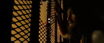 Movie still from “Hunger” (2008), directed by Steve McQueen – A man with a beard is looking through a fence; Close Up shot, Low angle