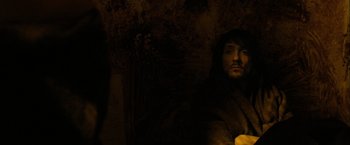 Movie still from “Hunger” (2008), directed by Steve McQueen – A man with long black hair and a beard is sitting in a dark room; Close Up shot, High angle