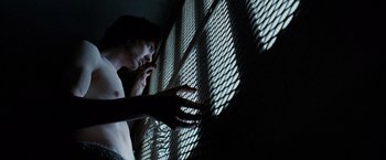 Movie still from “Hunger” (2008), directed by Steve McQueen – A man leaning against a metal fence with his hand on his chest; Close Up shot, Low angle